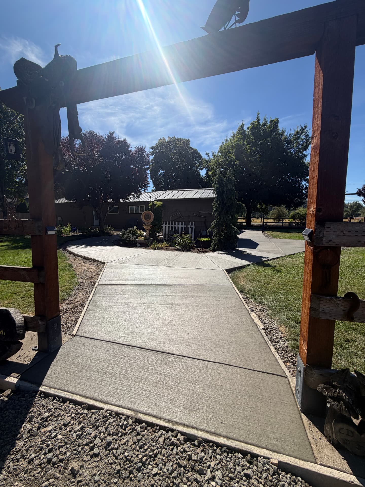 Broom-finished concrete walkway forking around a garden island beneath a timber arbor